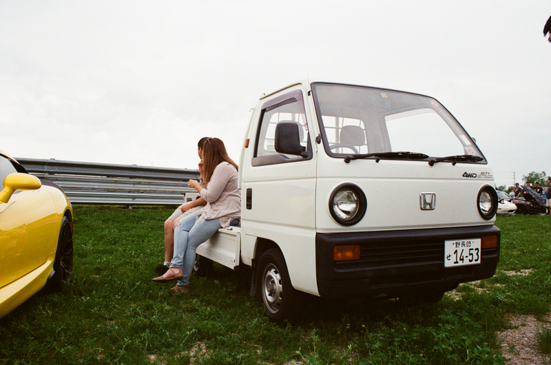 A couple of people having a moment on the bed of a kei truck complete with Japanese licensing stickers.